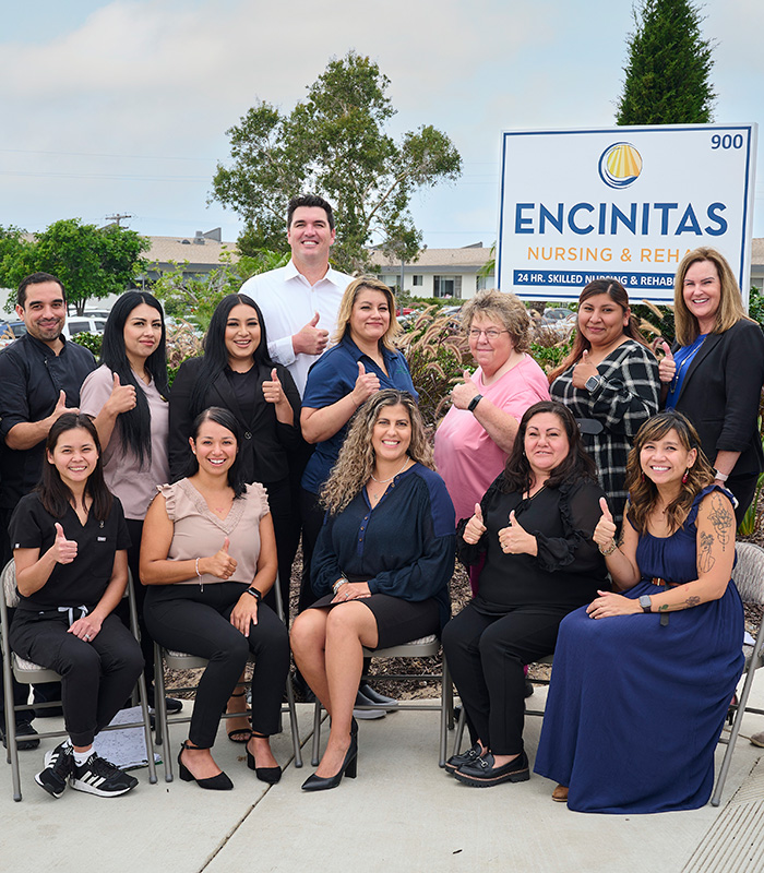 Team, staff, and executives at the front of the Encinitas Nursing and Rehab facility showing the sign