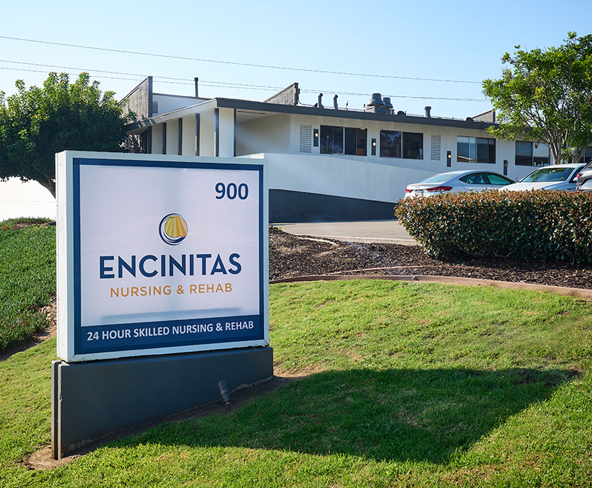 Front of the Encinitas Nursing and Rehab facility showing trees, green grass, and sign